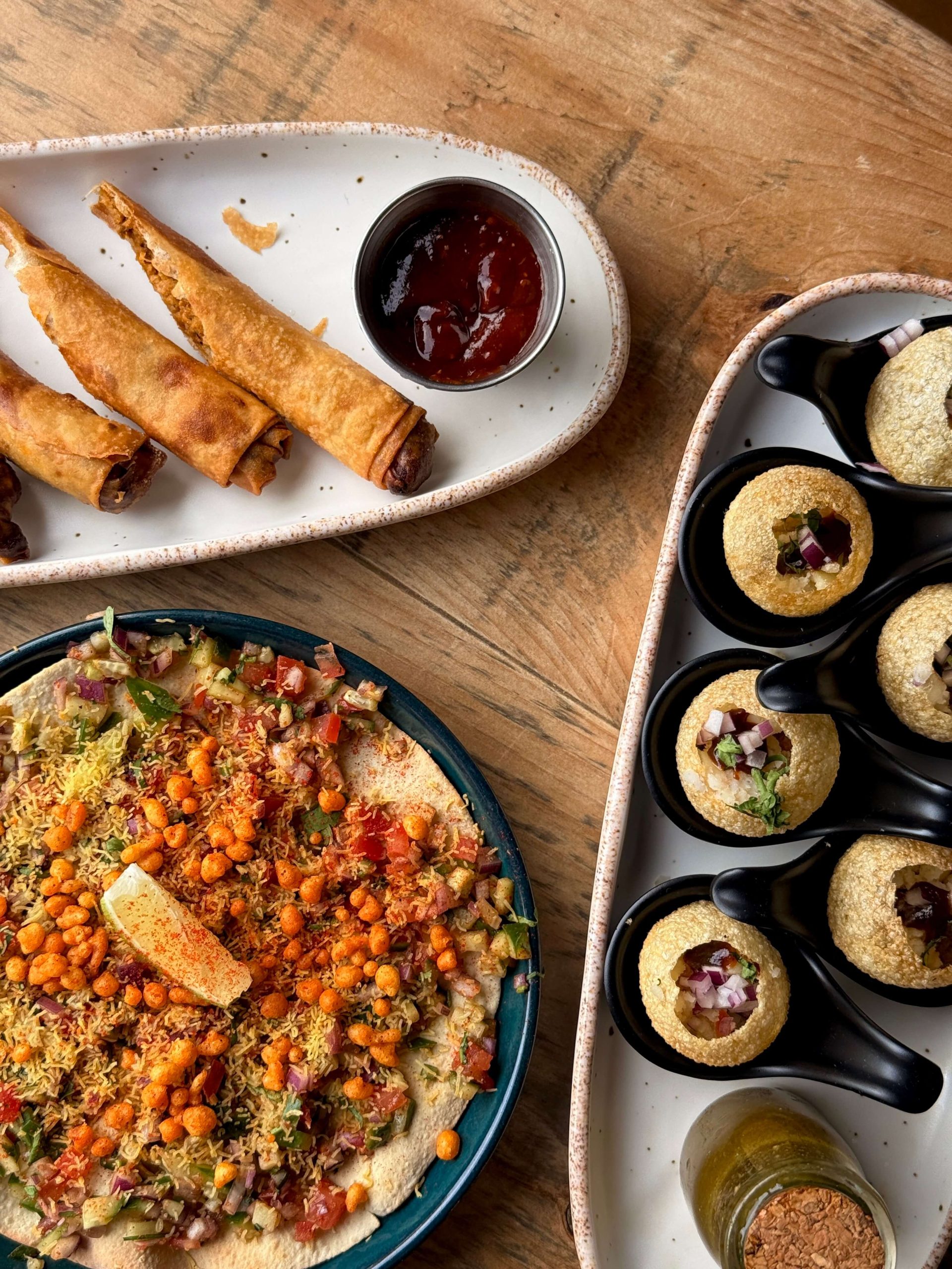 Assorted Indian street food snacks including crispy rolls, chaat, and pani puri on a wooden table.